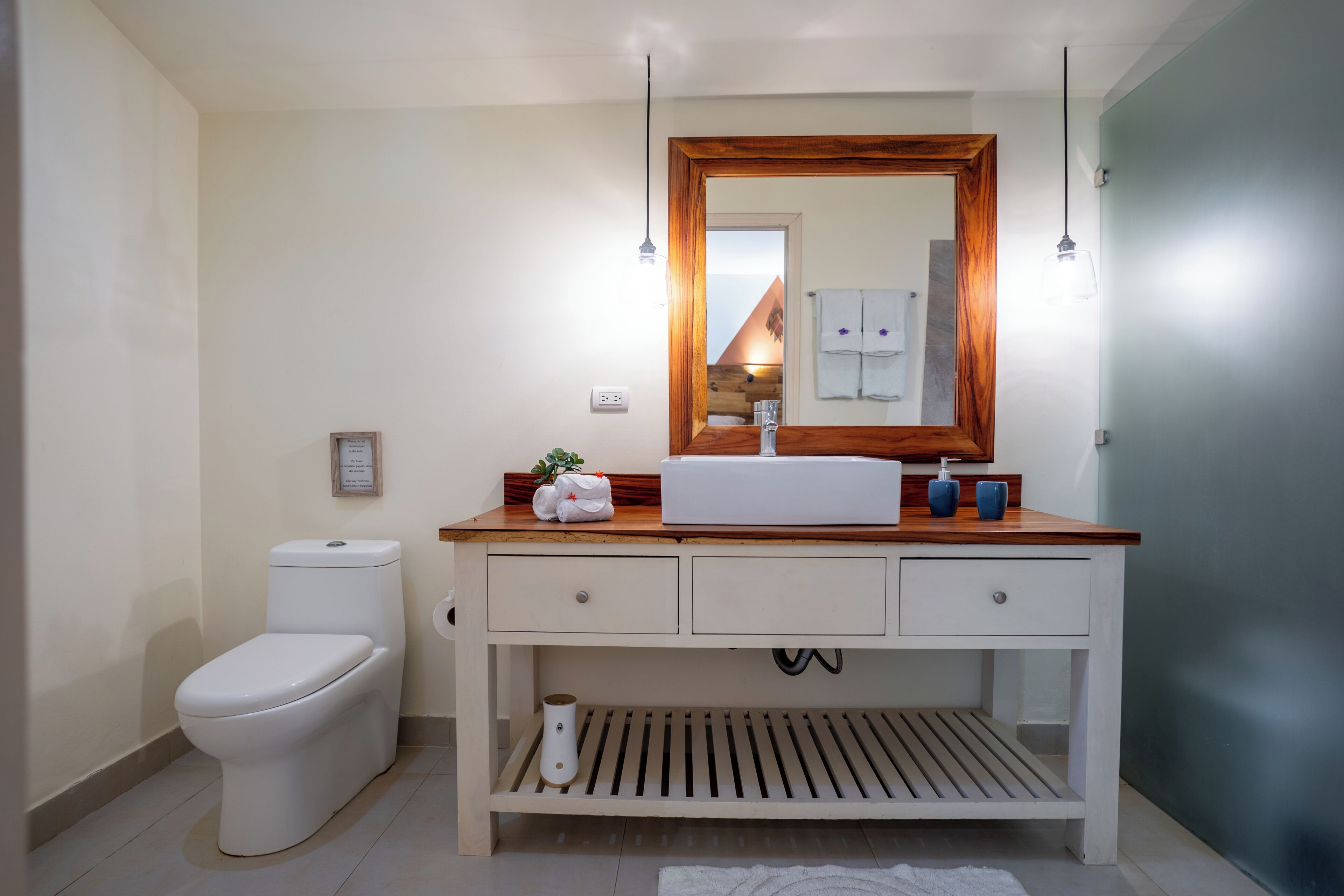 Un baño con inodoro blanco, tocador de madera con espejo y lavamanos.