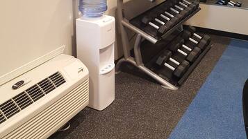 A fitness center with a water dispenser, air conditioning unit, and various exercise equipment.