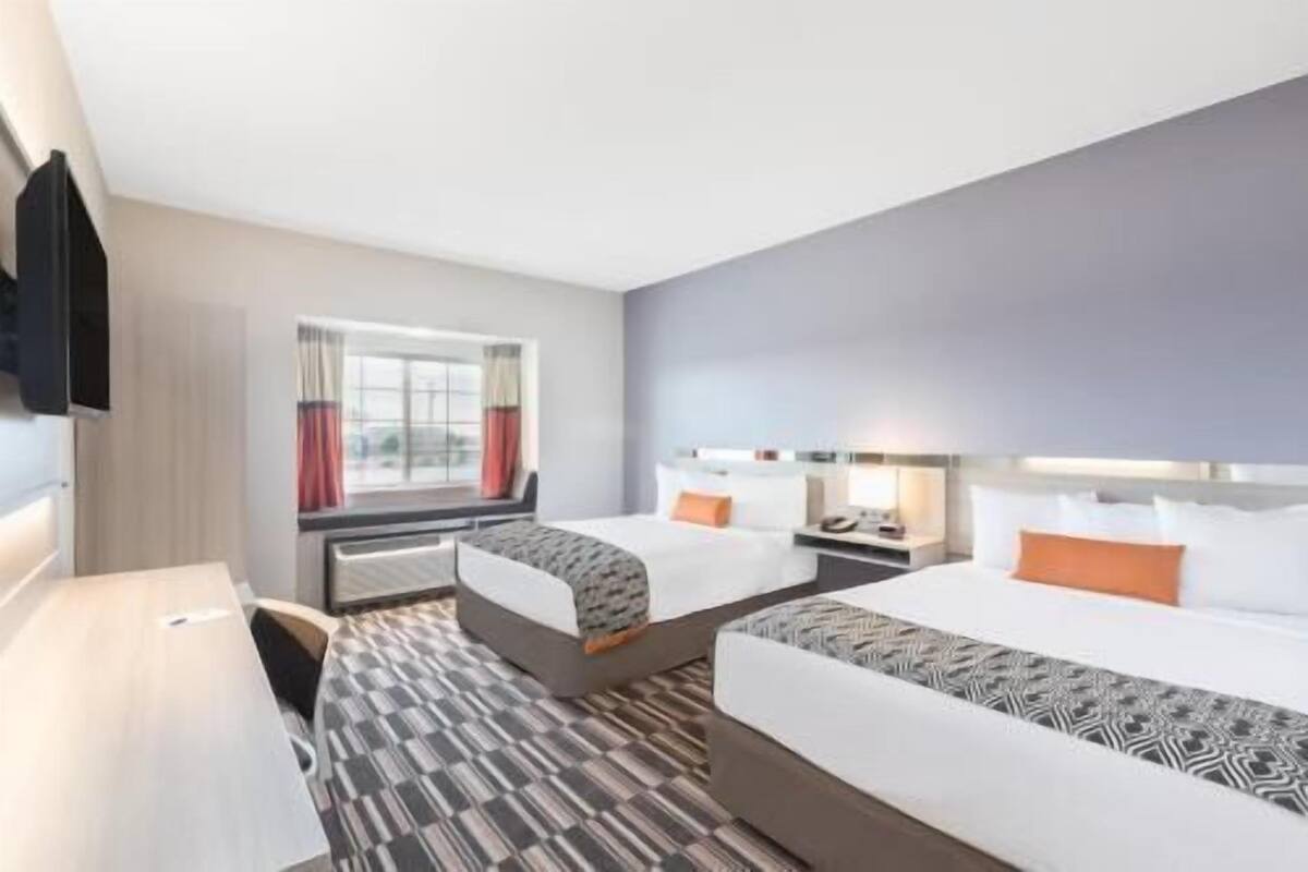 A hotel room with two beds, a desk, a window with curtains, and a patterned carpet.