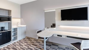 Una habitación de hotel moderna con kitchenette, un televisor de pantalla plana montado en la pared, una mesa de comedor con sillas y un suelo estampado.