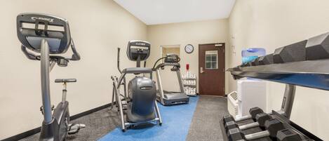 Un gimnasio con máquinas de cardio, mancuernas y un dispensador de agua.