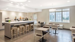 Un área de cocina moderna con una isla central, taburetes de bar y una zona de comedor con mesas y sillas.