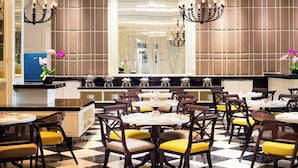 Un restaurante con mesas redondas, sillas con cojines amarillos y piso a cuadros.
