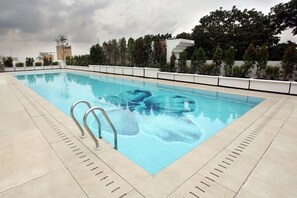 Una piscina rectangular con superficie de agua cristalina y azul, rodeada por un bordeado de baldosas.