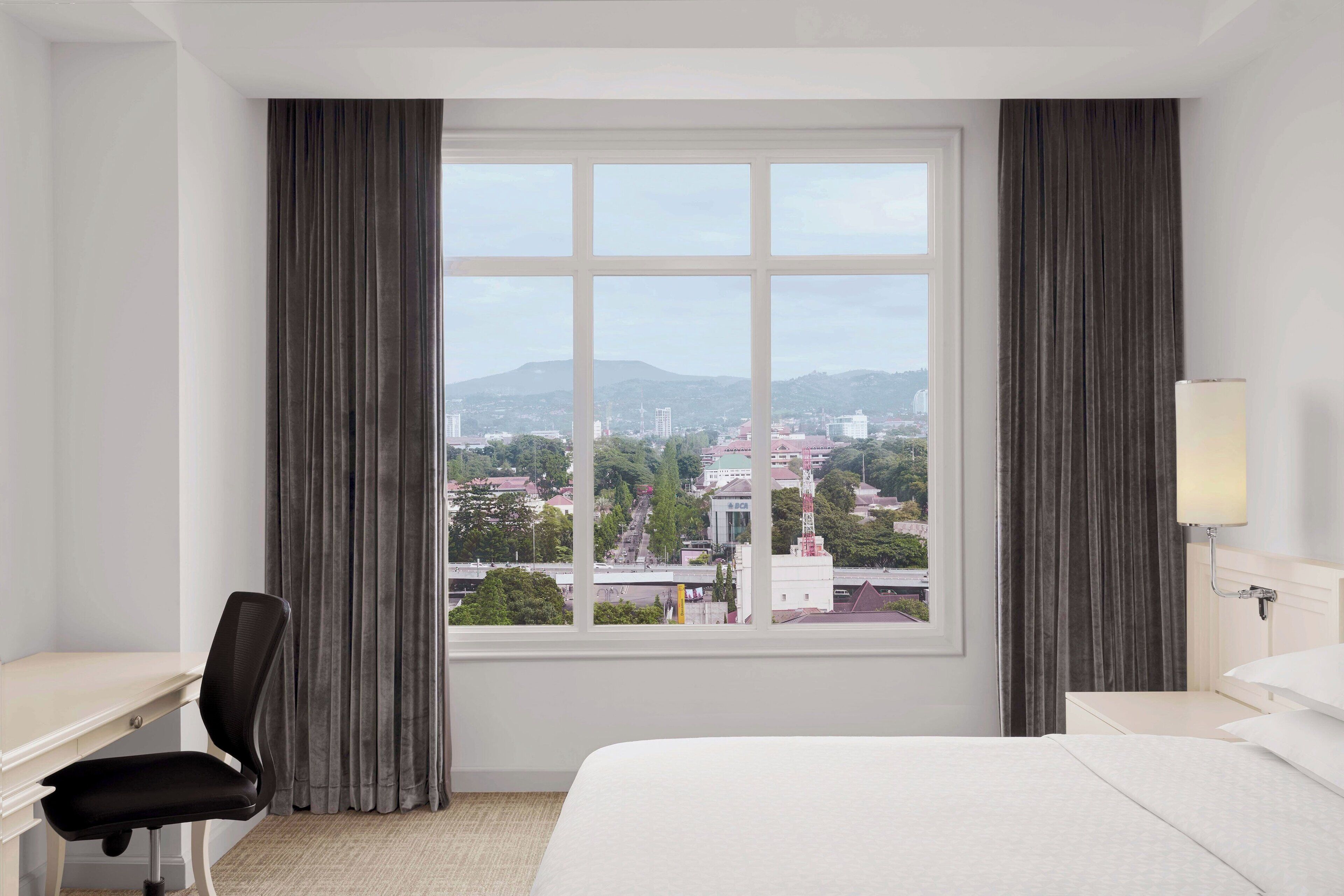 Habitación de hotel con un ventanal grande, una cama, un escritorio y una silla.