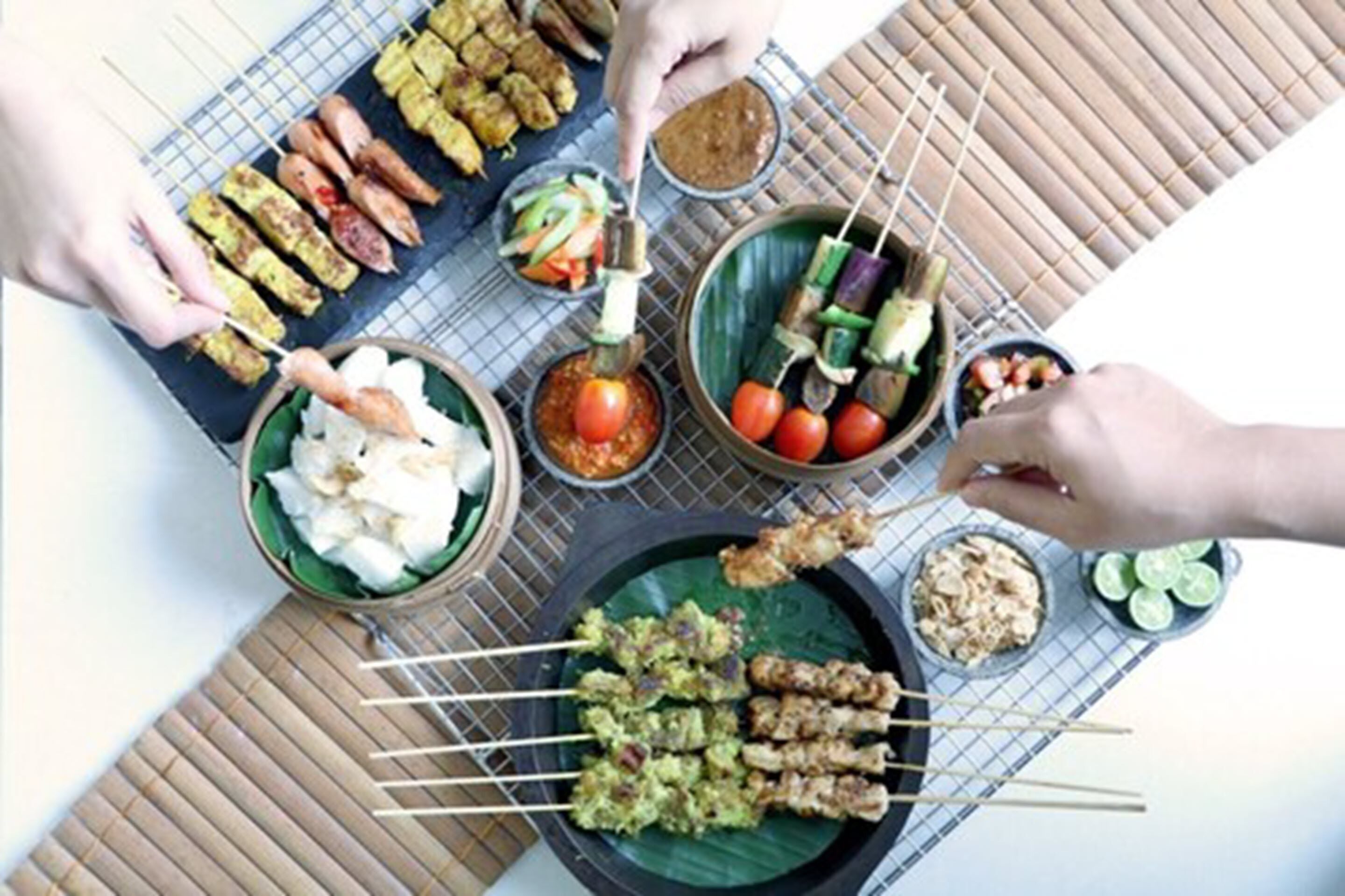 Une variété de viandes et de légumes en brochettes, présentés sur une table avec des bols contenant des sauces et des accompagnements.