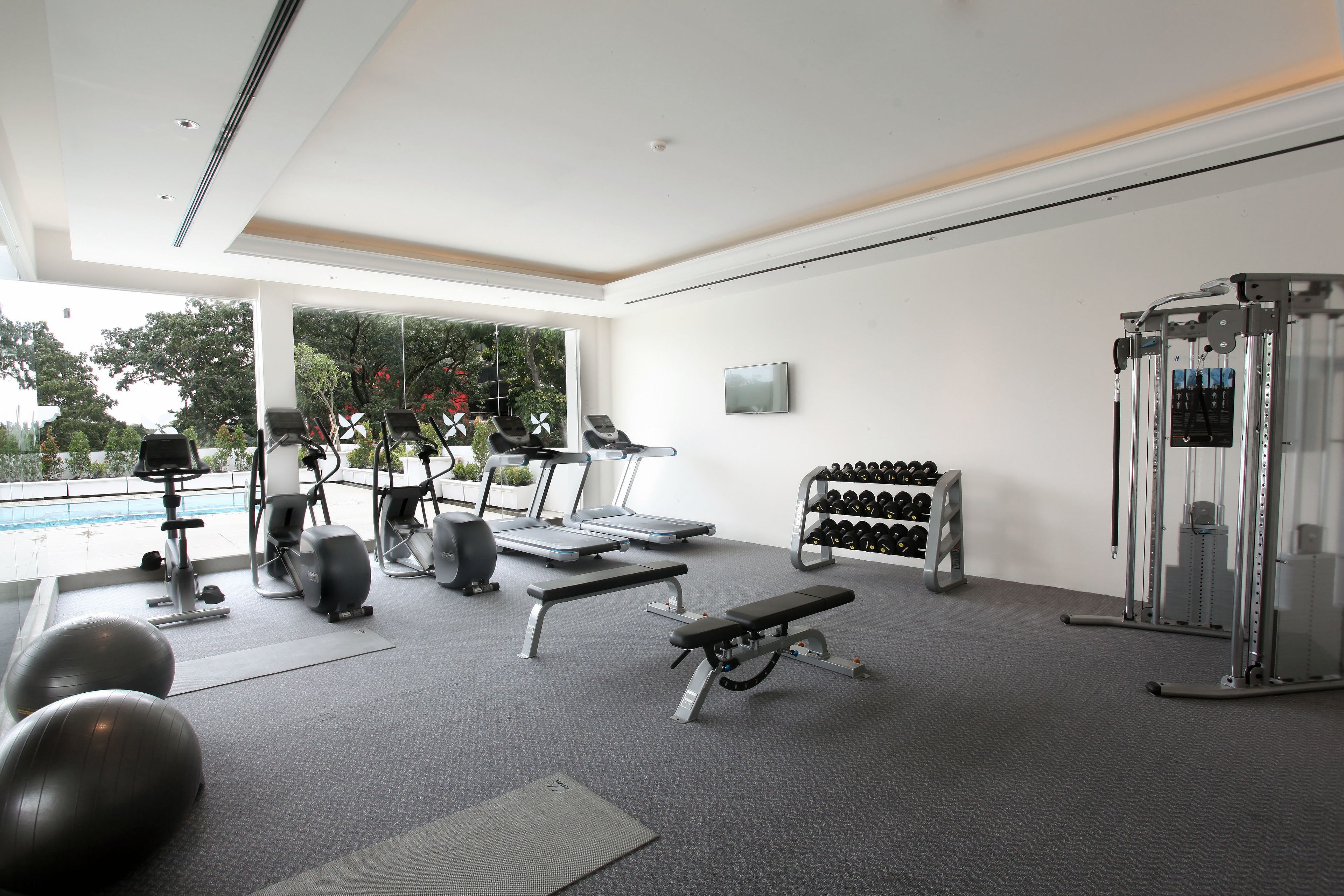 Un gimnasio con equipo de ejercicio, una banca y una estantería con mancuernas.