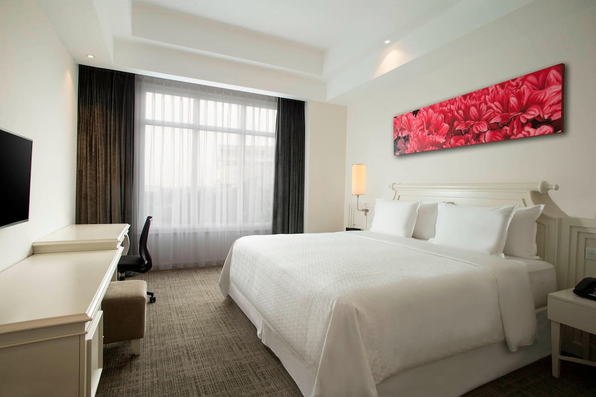 Habitación de hotel con una cama grande, un escritorio, una silla, un televisor y un cuadro en la pared.