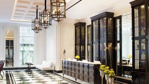 Un hall de hotel con suelo a cuadros, un sofá blanco, una consola negra con jarrones y armarios grandes de color negro.