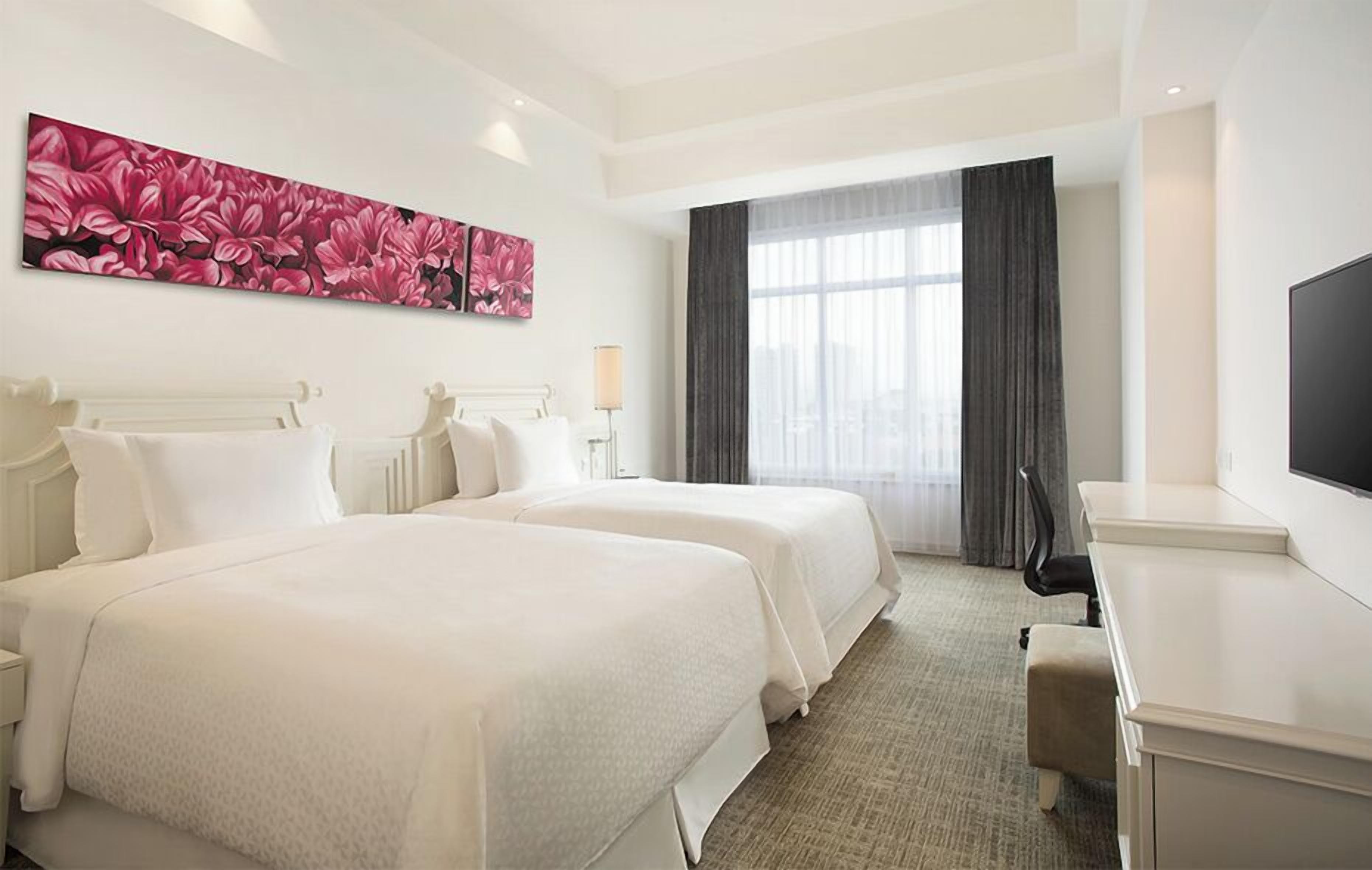 Una habitación de hotel con dos camas, un escritorio, un televisor y un cuadro grande con motivos florales en la pared.
