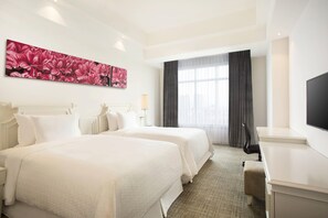 Habitación de hotel con dos camas, un escritorio, un televisor y una gran obra de arte floral en la pared.