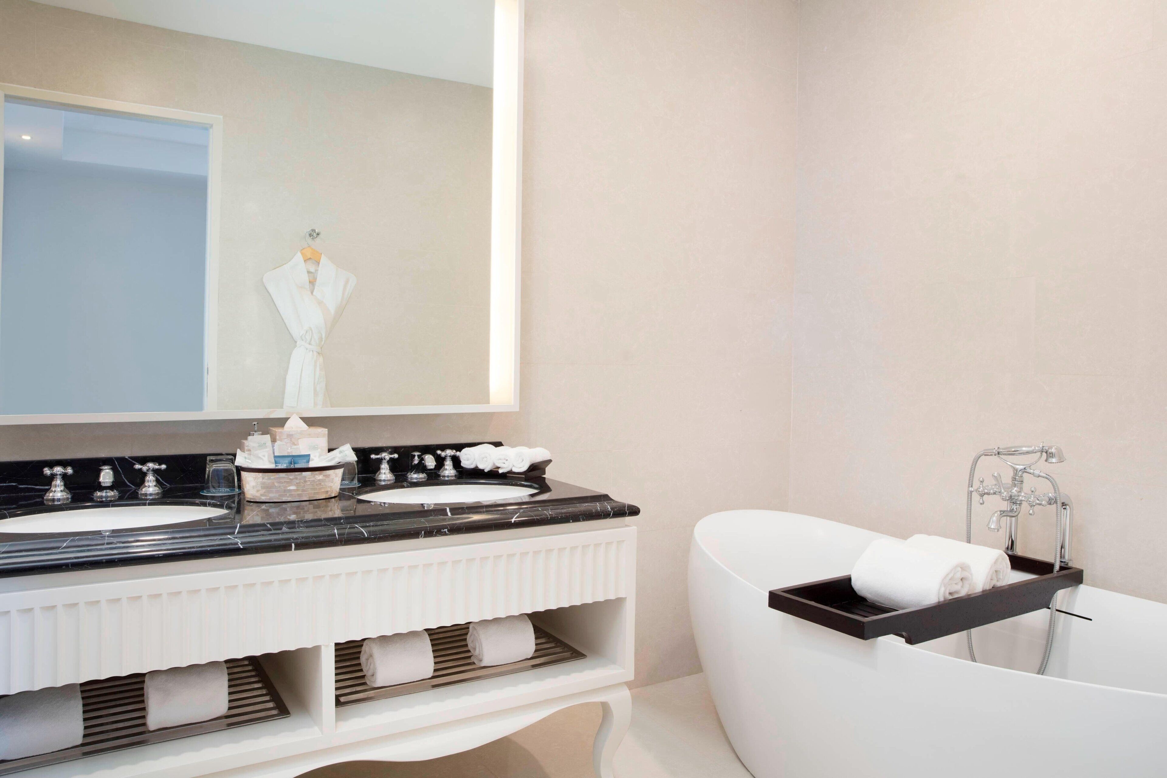 Un baño moderno con dos lavamanos, un espejo grande, una bañera y un perchero para toallas.
