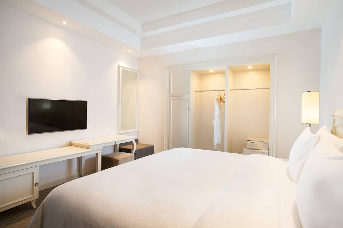 Habitación de hotel con una cama grande, un televisor de pantalla plana montado en la pared, un tocador con espejo y un vestidor con bata colgada.