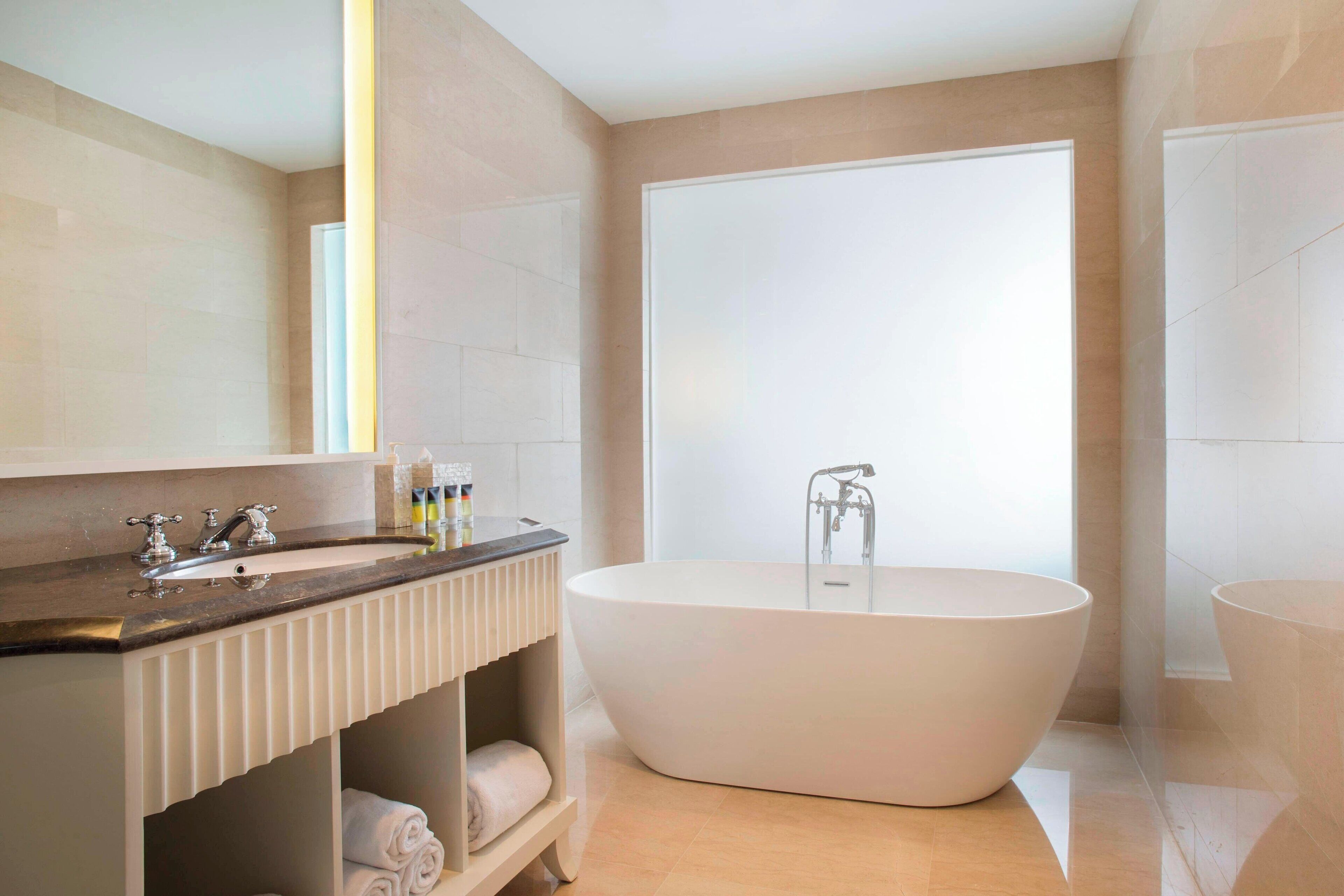 Un baño moderno con una bañera independiente, un tocador con encimera oscura y un espejo grande.