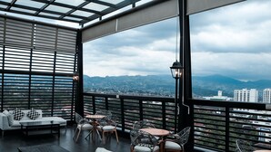 Una terraza en la azotea con vistas a la ciudad, amueblada con un sofá, sillas y mesas.