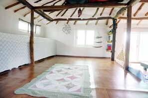 A room with a wooden ceiling, a quilt on the floor, a window, and a shelf with items.