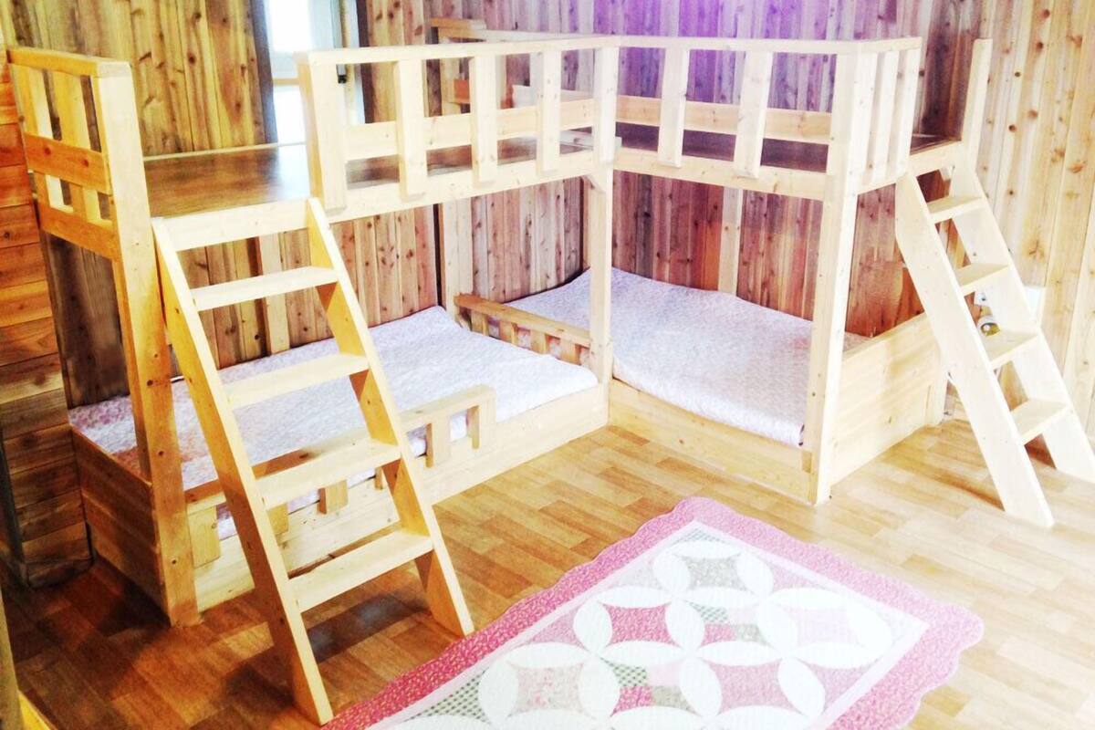 A wooden bunk bed with a ladder, a small table, and a pink patterned rug.