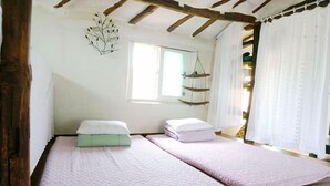 Une chambre avec deux lits, des poutres en bois, une plante suspendue et une fenêtre avec des rideaux.