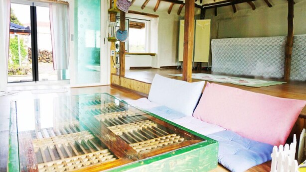 Une pièce avec une table à plateau en verre, un canapé avec des coussins, un lit à motifs et un plafond en bois.