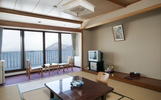 A room with a large window overlooking a body of water and mountains, a wooden table, a television, and a framed picture on the wall.
