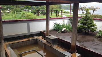 A covered outdoor hot tub area with a view of a landscaped garden and a body of water.