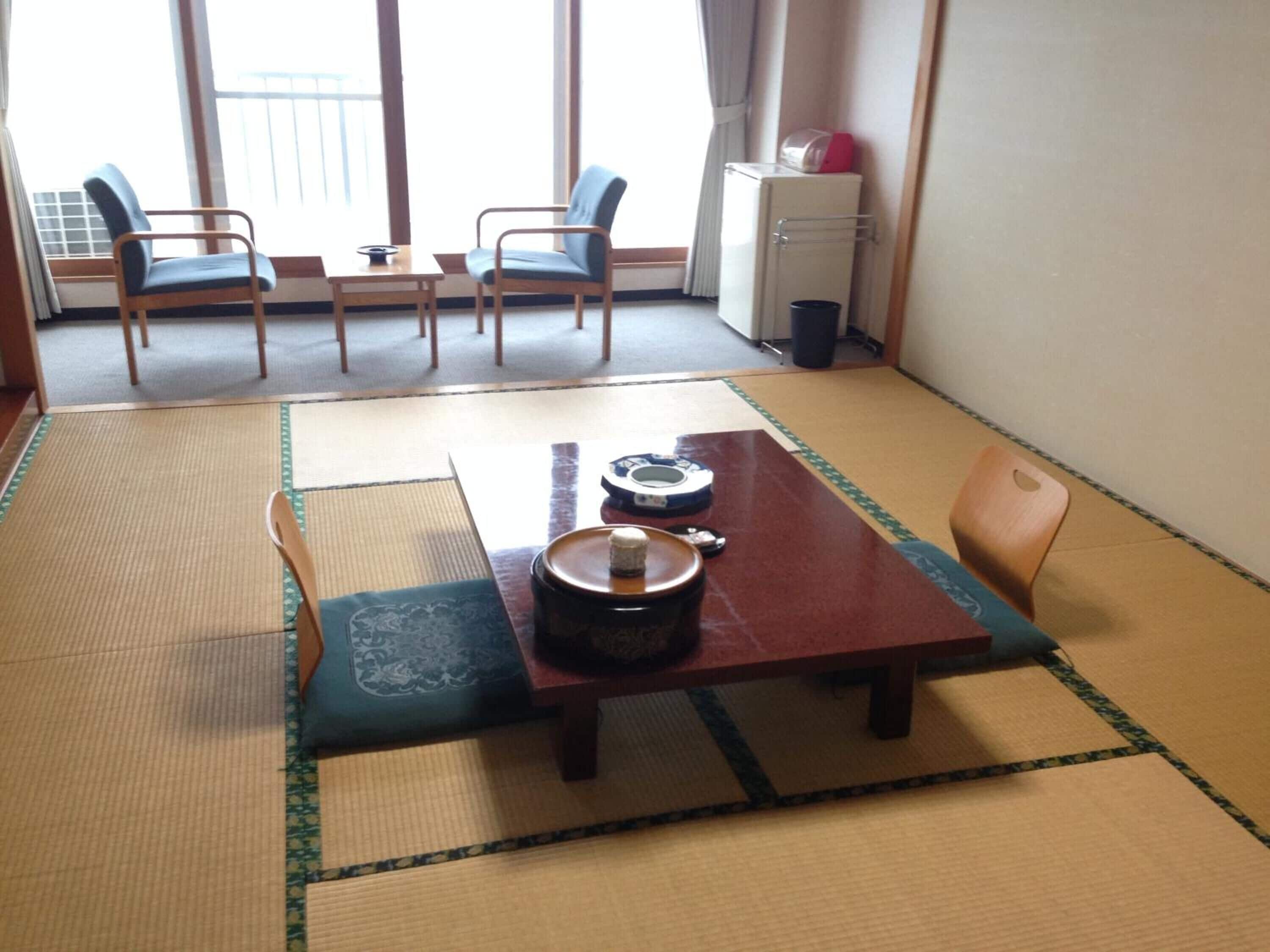 A traditional Japanese room with tatami flooring, a low table with a tea set, and two chairs.