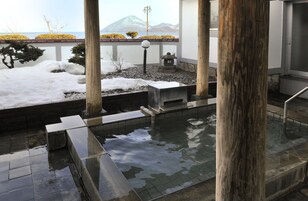 A traditional Japanese onsen with a stone hot spring, wooden pillars, and a view of snow-covered mountains.