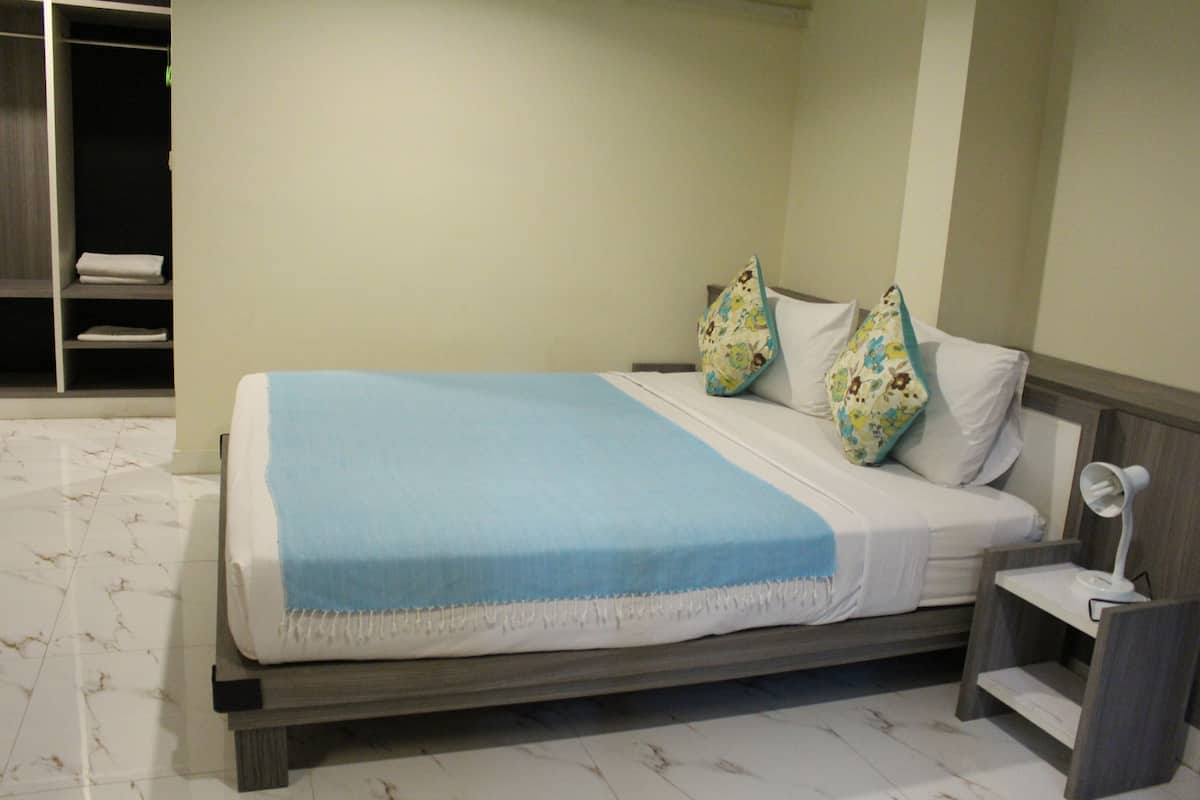 A neatly made bed with a blue blanket, two patterned pillows, and a bedside table with a lamp.