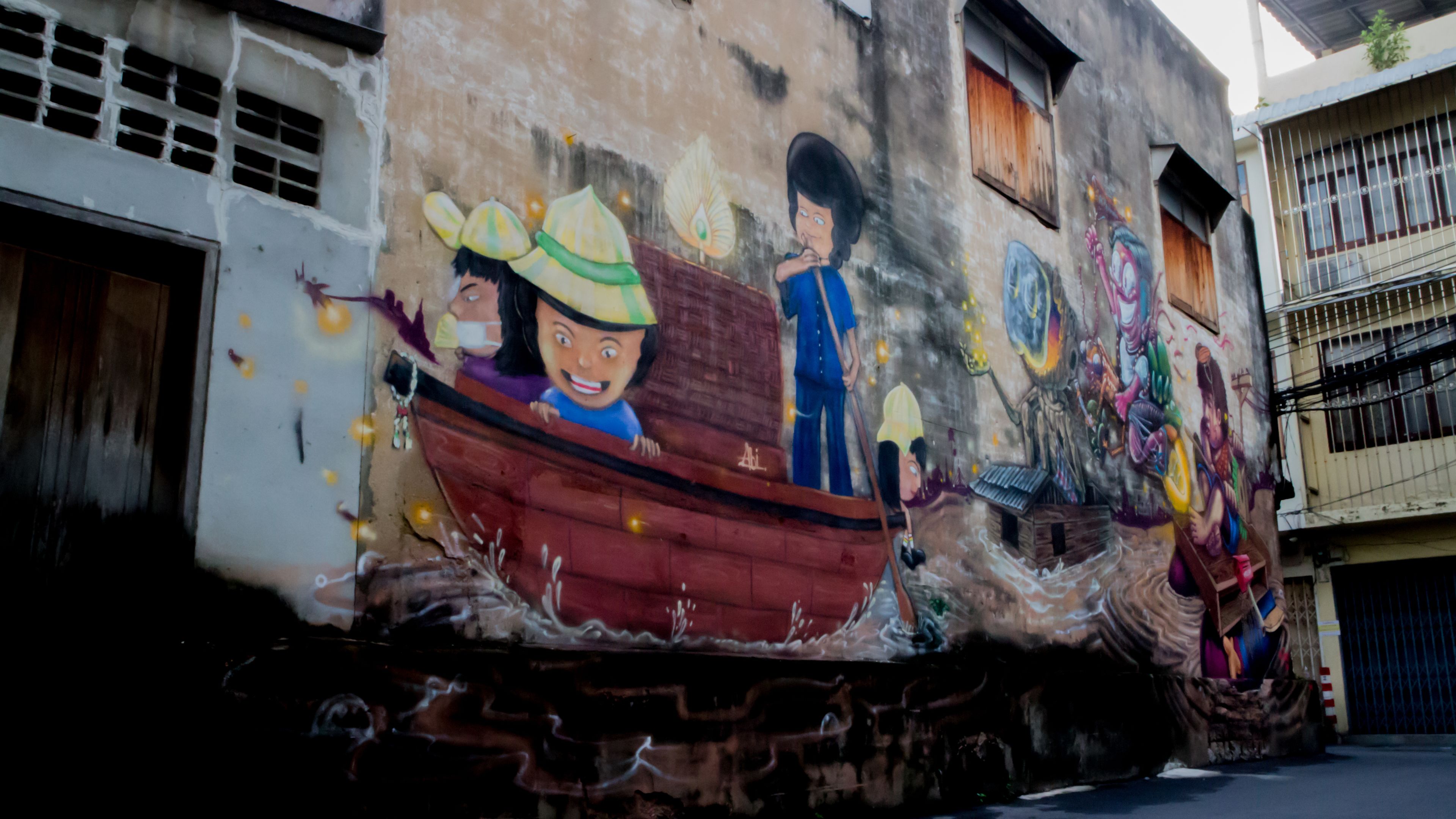 A mural on a building wall depicting a boat with people and a figure on a tree.