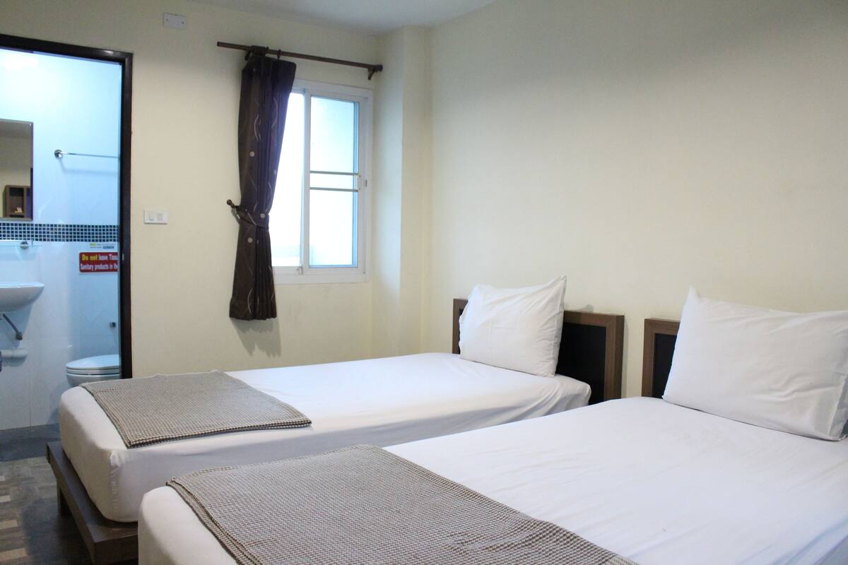 A hotel room with two beds, a window with curtains, a sink, and a mirror.