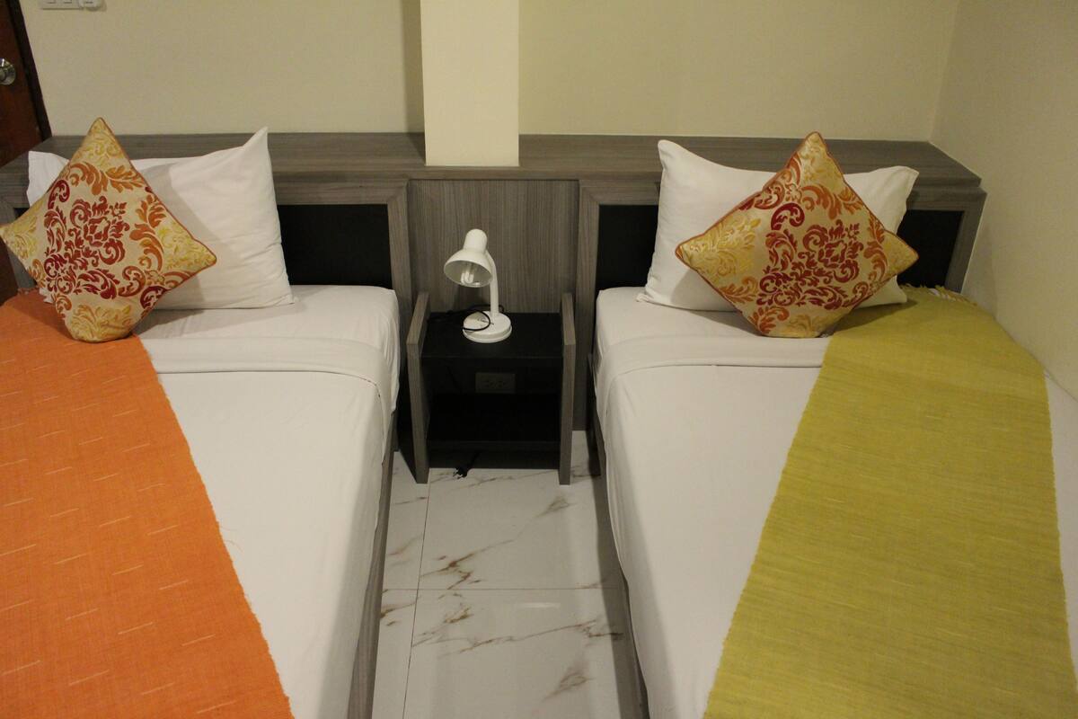 A hotel room with two single beds, each with a pillow and a bedside table with a lamp.