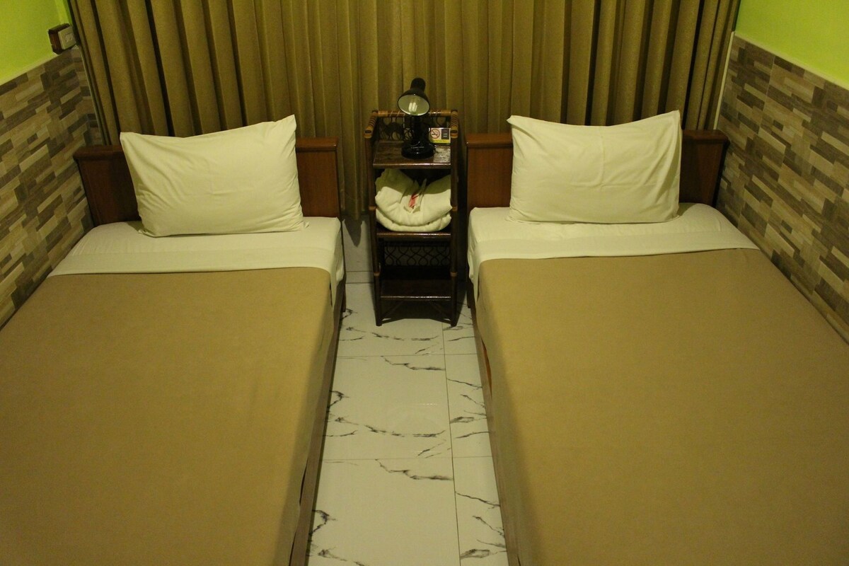 Habitación de hotel con dos camas, una mesita de noche con lámpara y un telón de fondo.