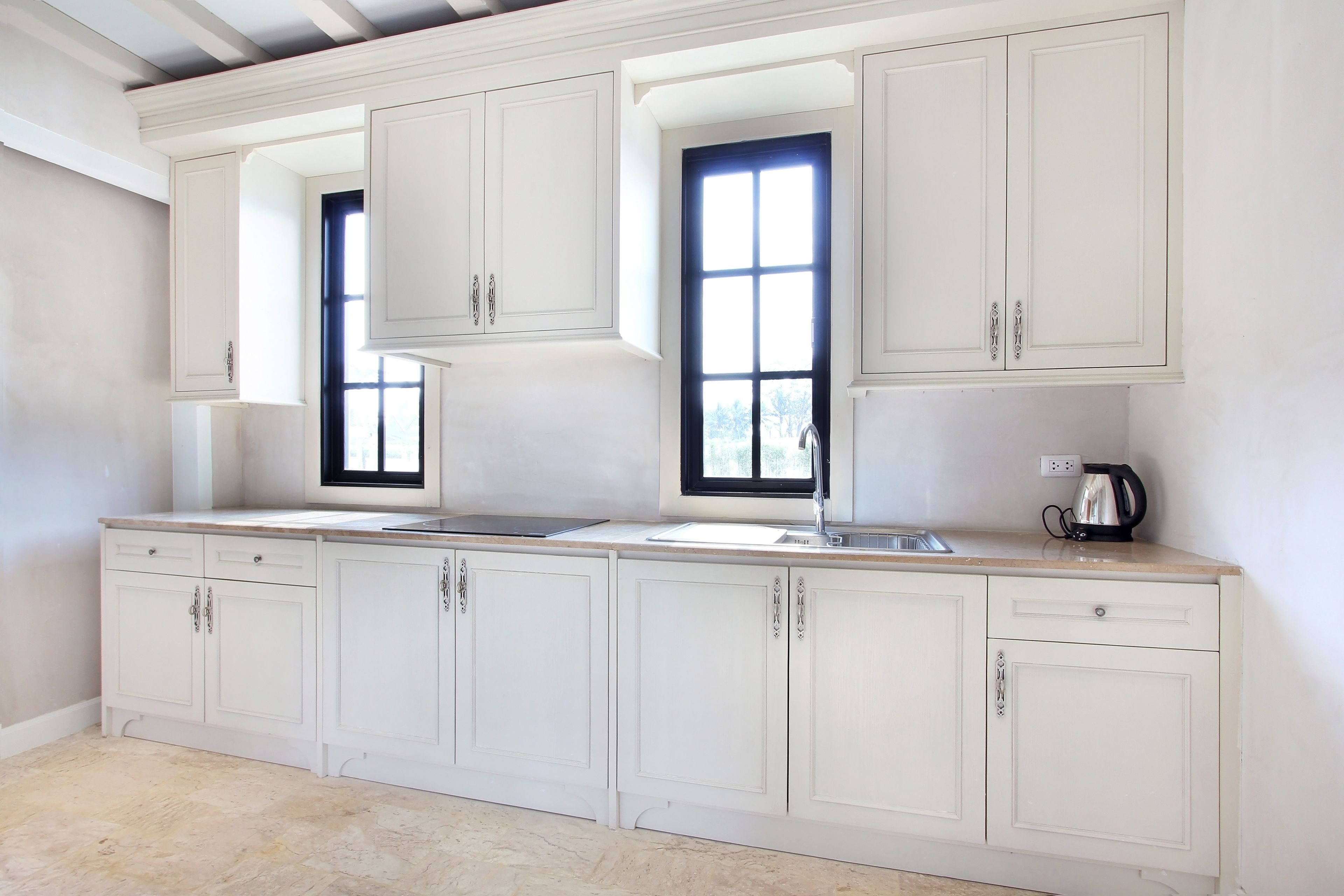 A kitchen with white cabinets, a window, a sink, and a kettle.