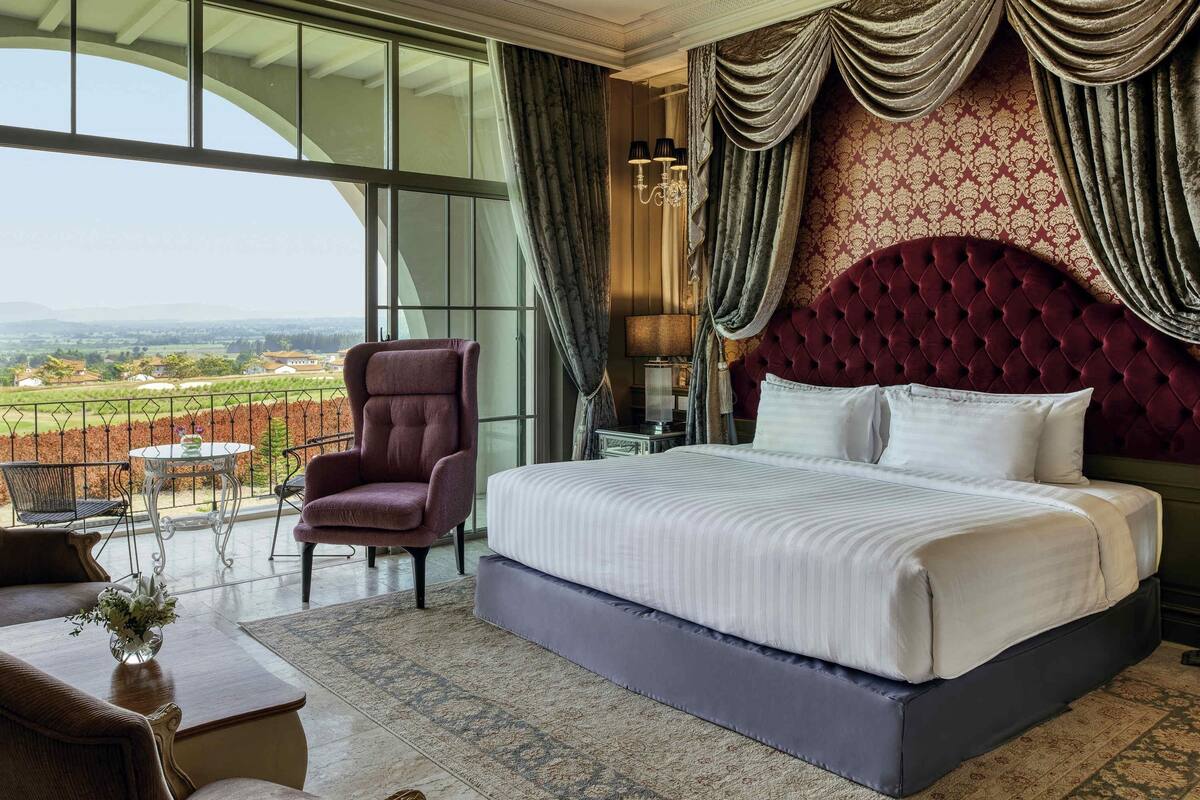 A bedroom with a large bed, a chair, a table, and a view of the countryside.