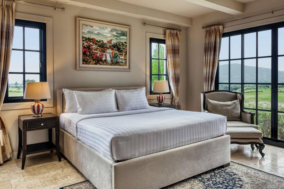 A bedroom with a large bed, two bedside tables, a chair, and a painting on the wall.