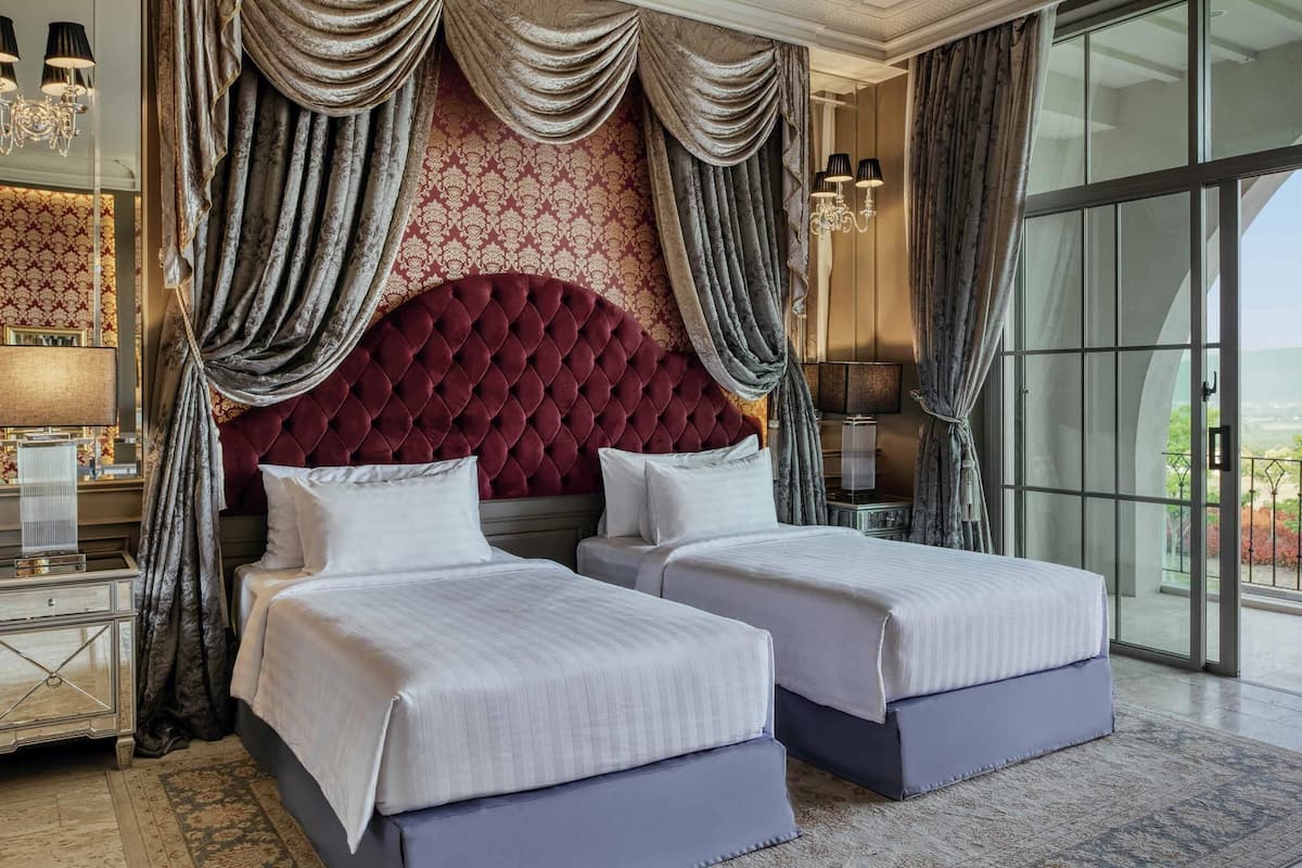 A hotel room with two beds, a large tufted headboard, and a view through a glass door.