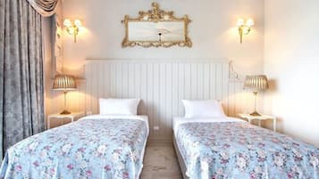 A hotel room with two beds, floral bedding, a white radiator, and wall-mounted lamps.