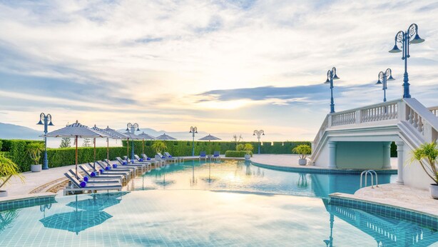 A pool with lounge chairs and umbrellas, a staircase, and a building with a balcony. - Mövenpick Resort Khao Yai (Pak Chong)