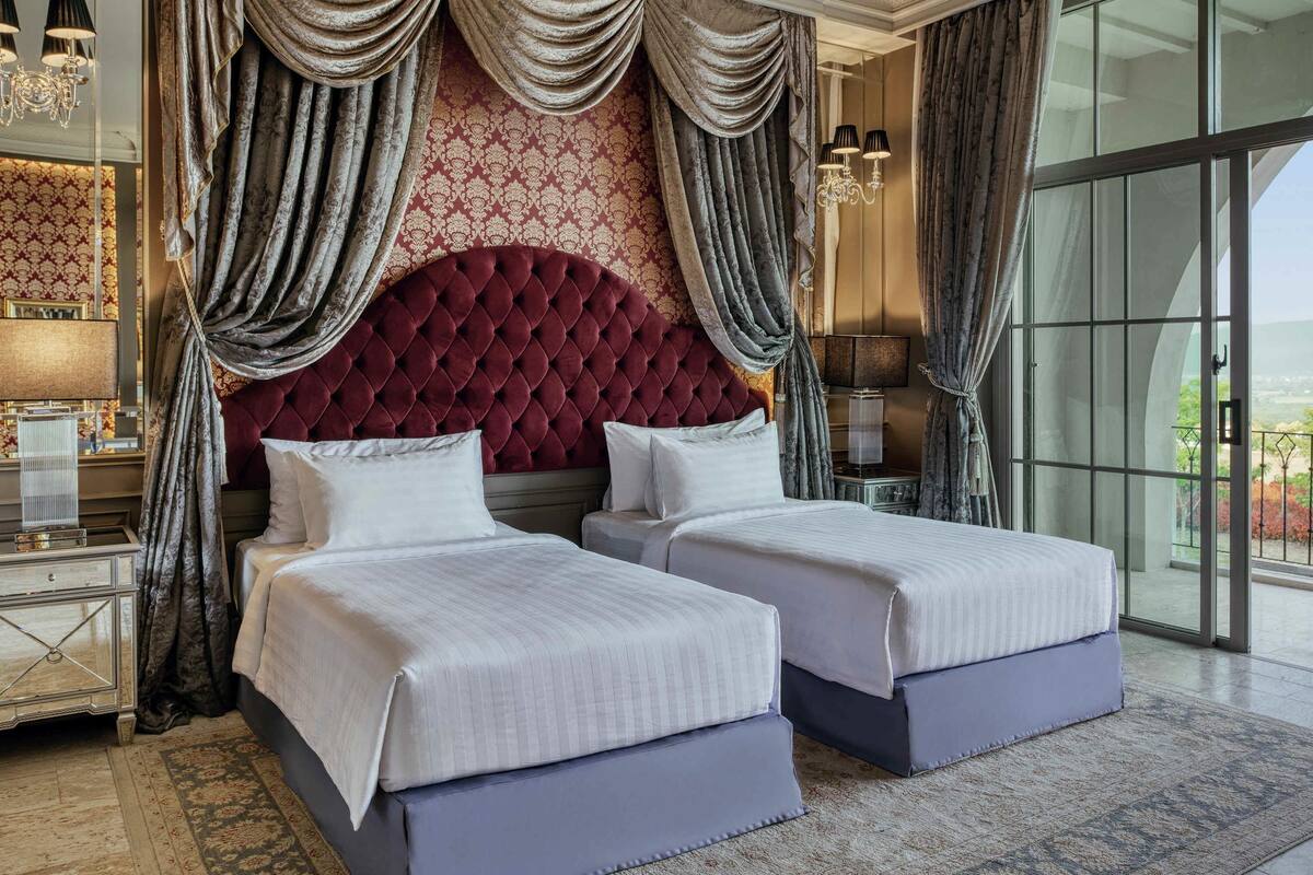 A hotel room with two beds, a large tufted headboard, and a view through a glass door.