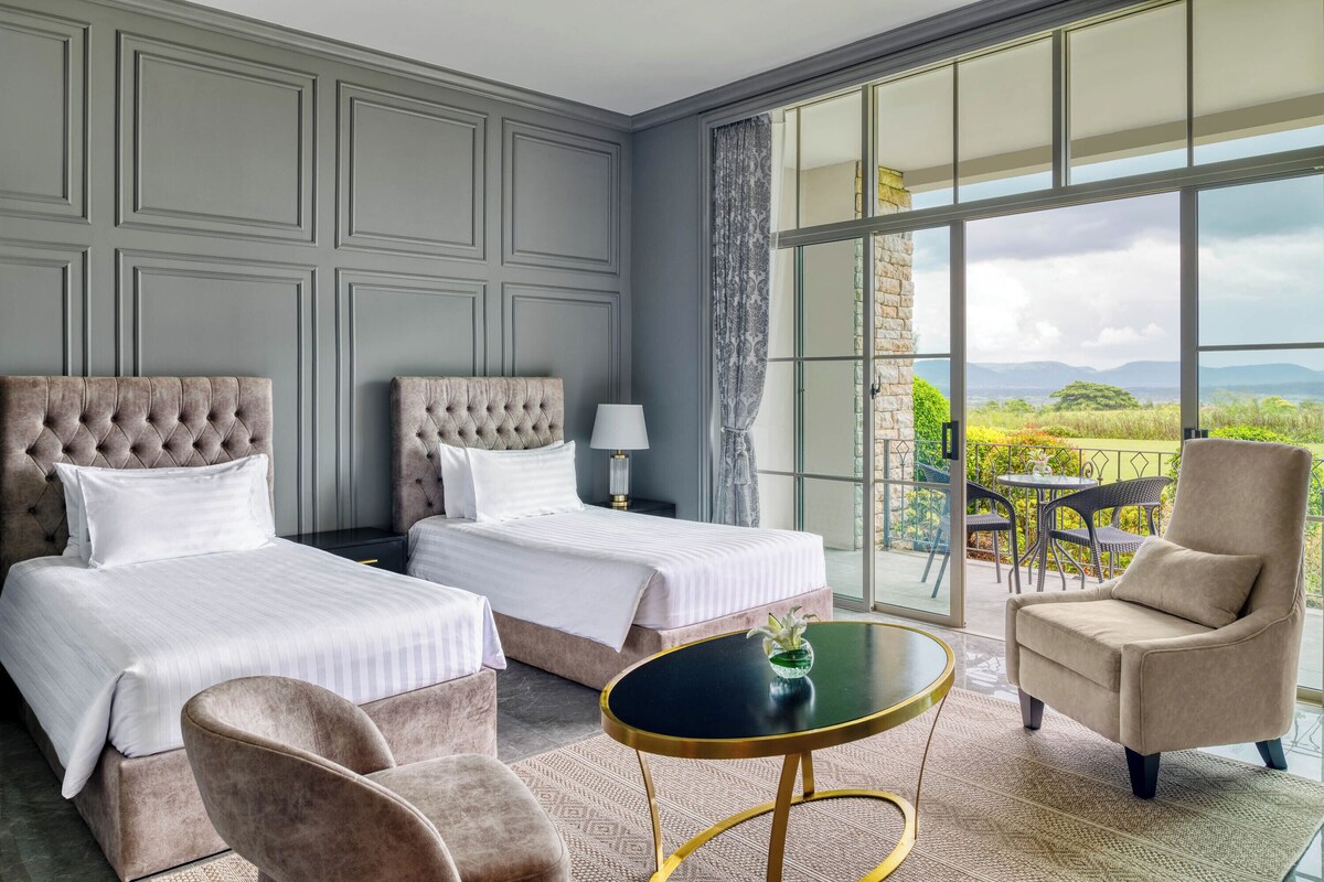 Une chambre d’hôtel avec deux lits, une table ronde, une chaise et une vue sur l’extérieur.