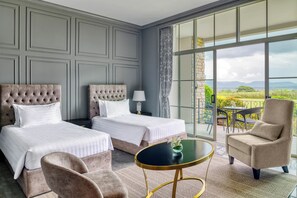 A hotel room with two beds, a round table, a chair, and a view of the outdoors.