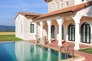 A poolside area with a clear view of the pool, a patio with outdoor furniture, and a stone building with arches. - Mövenpick Resort Khao Yai (Pak Chong)