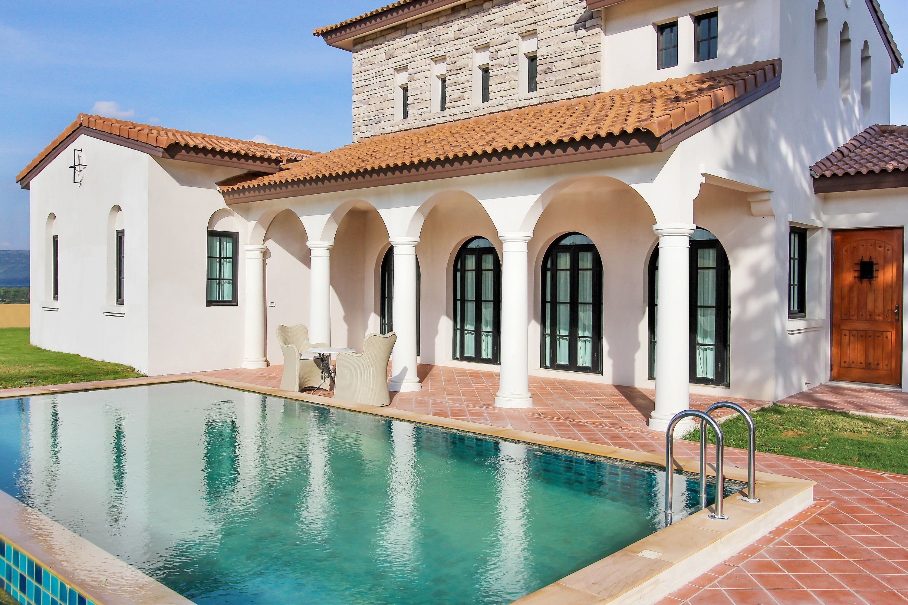 A large house with a swimming pool, white walls, and a tiled roof.