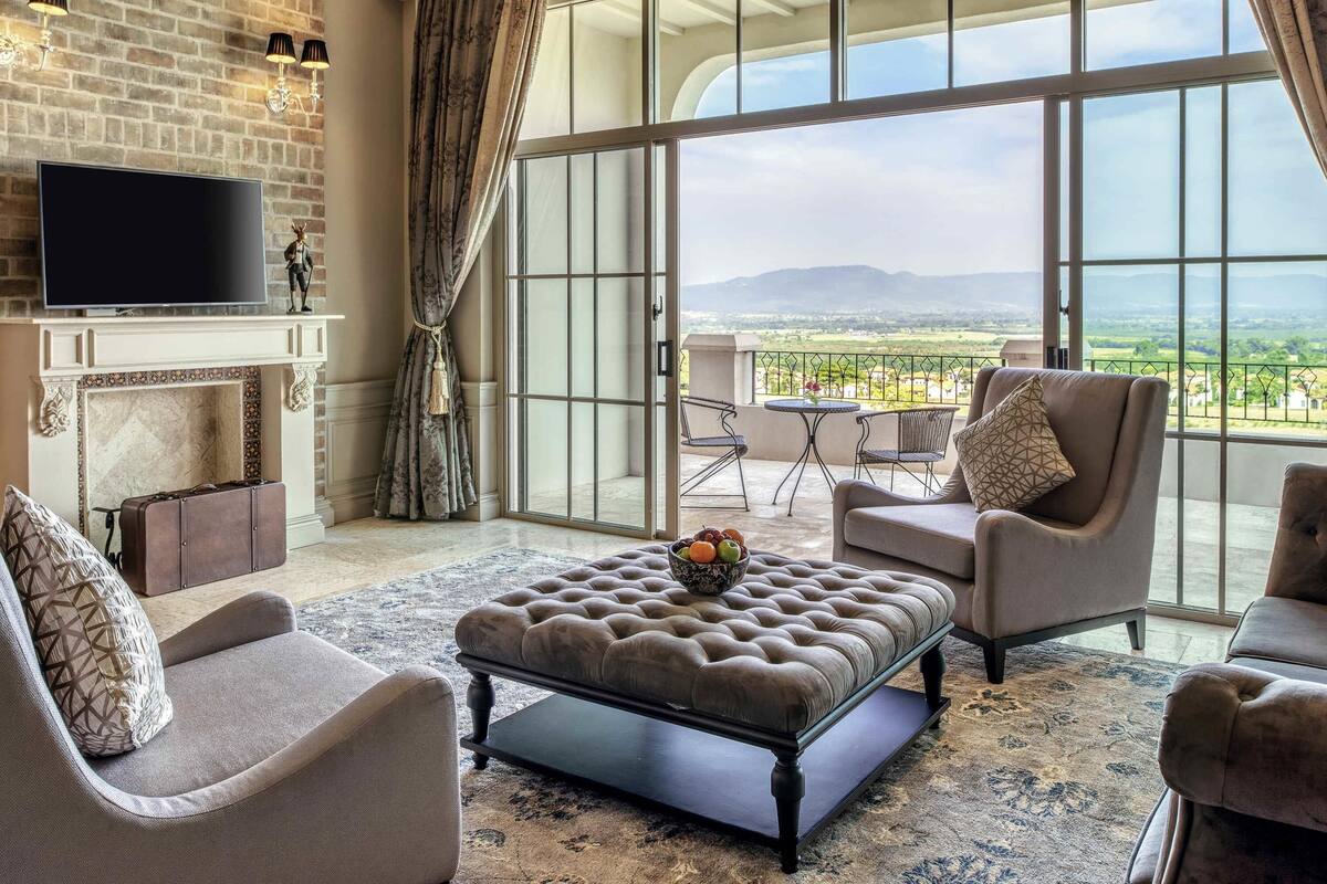A spacious living room with a fireplace, a television, and a balcony with a view of the countryside.
