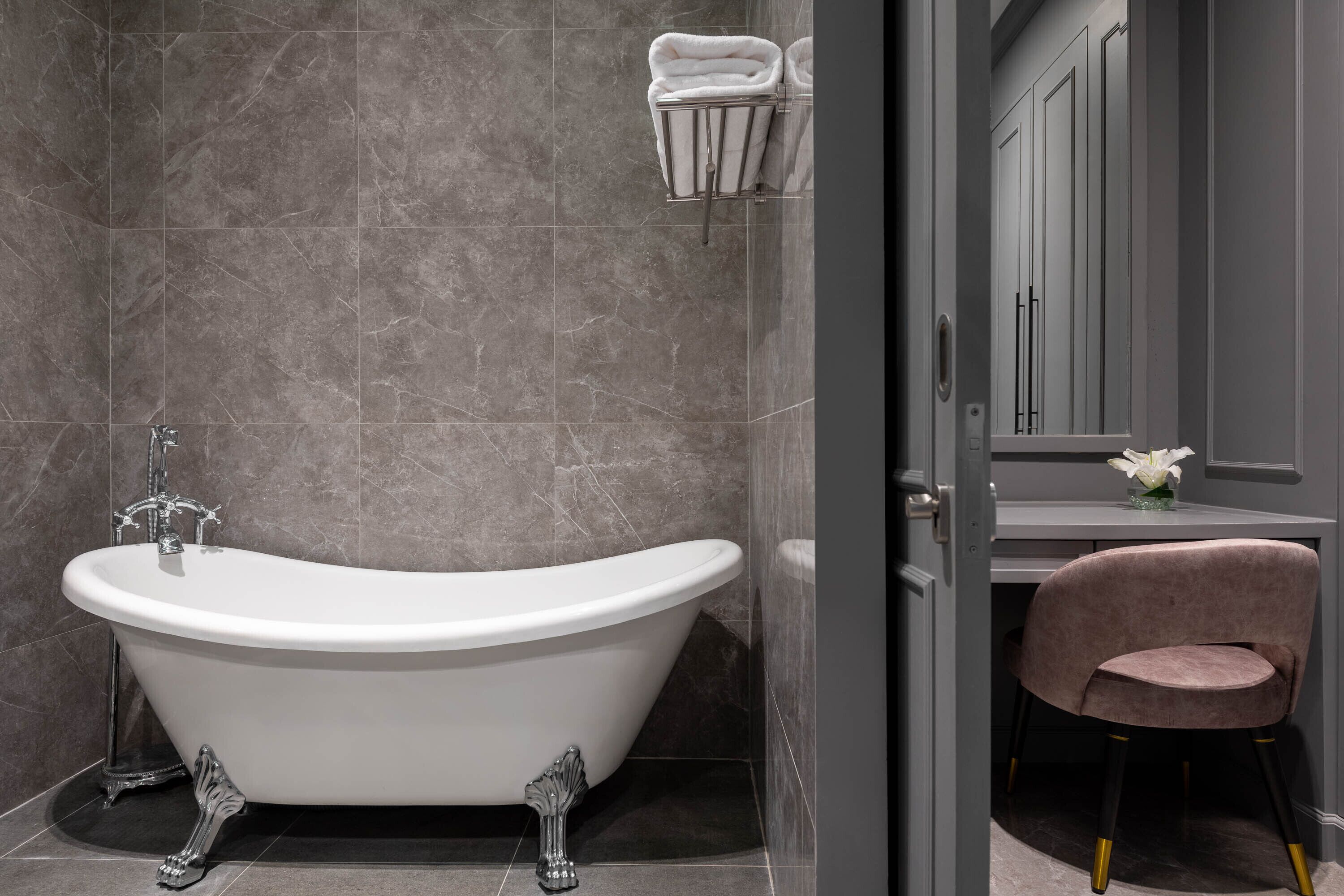 A modern bathroom with a freestanding bathtub, a vanity with a mirror, and a chair.