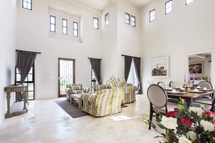 A spacious living room with high ceilings, a dining area, and a view of the outdoors.