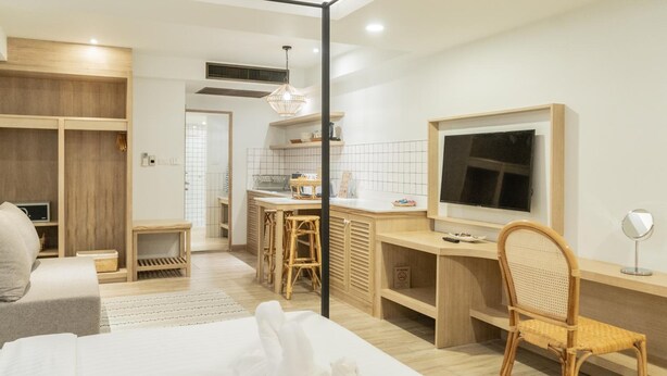 A modern hotel room with a bed, a desk, a chair, a television, and a kitchenette. - Amaka Bed & Breakfast (Chiang Mai)