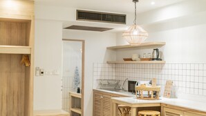 A modern kitchen with wooden cabinets, a white tiled backsplash, a hanging light fixture, and a small island with stools. - Amaka Bed & Breakfast (Chiang Mai)