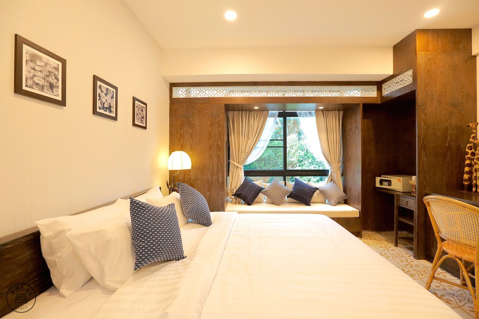 Une chambre d’hôtel avec un grand lit, un coin fenêtre aménagé en siège, un bureau et une lampe.