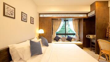 Une chambre d’hôtel avec un grand lit, un coin fenêtre aménagé en siège, un bureau et une lampe.